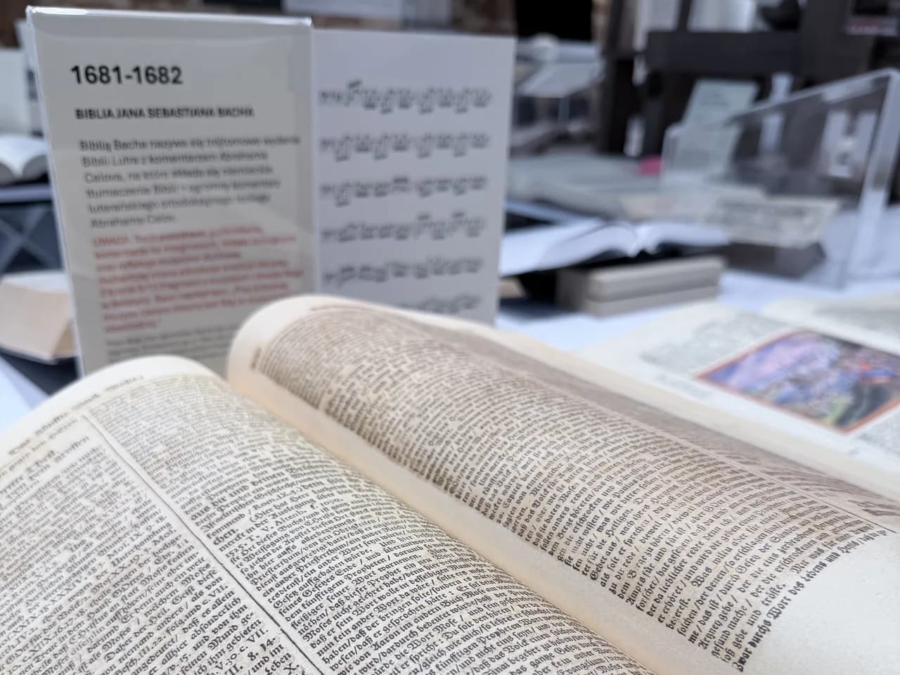 Otwarta Biblia Jana Sebastiana Bacha, za nią tabliczka z opisem i kartą z zapisem nutowym.