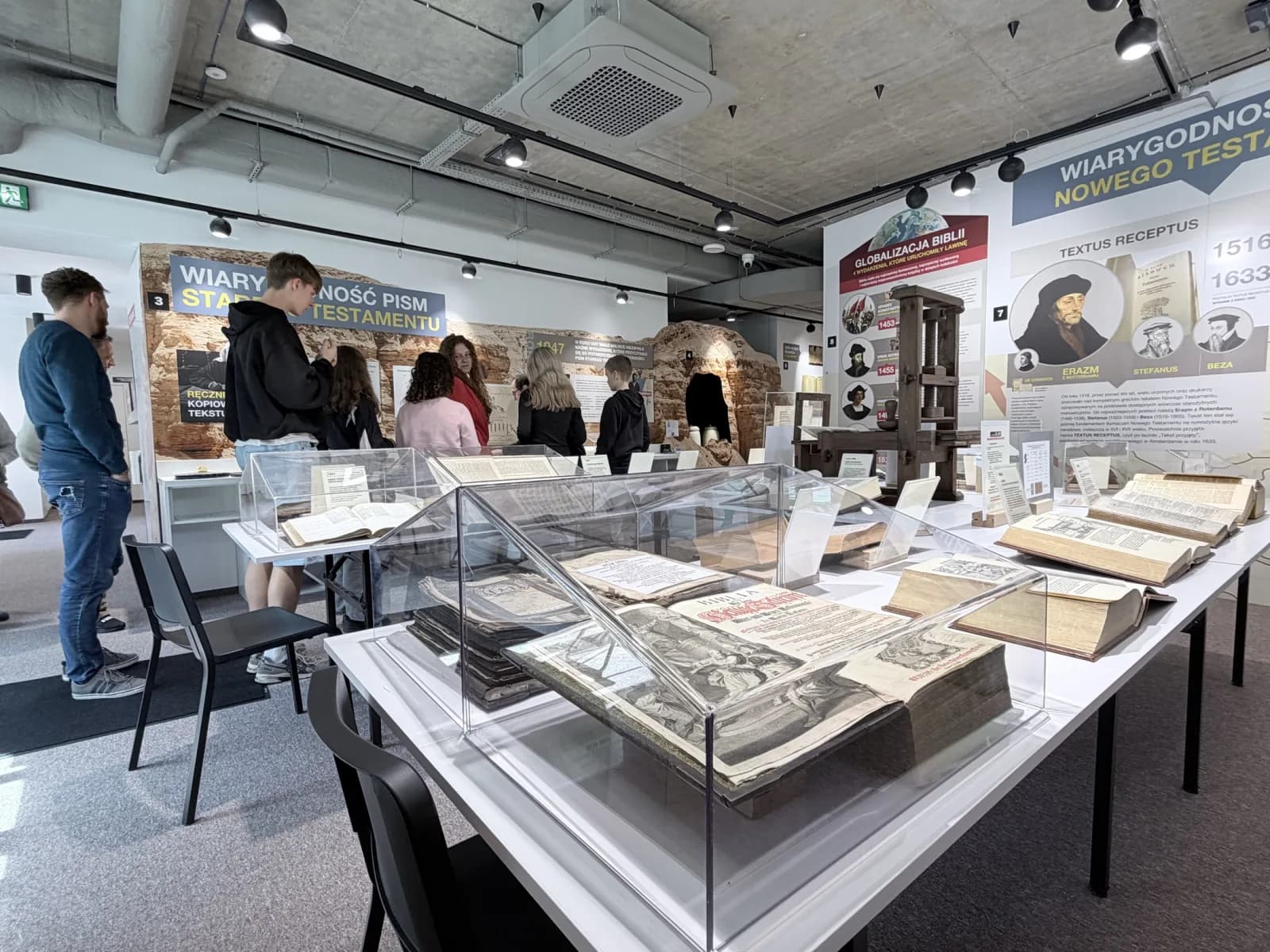 Sala wystawowa Muzeum Biblii w Ustroniu ze zwiedzającymi przy gablotach.