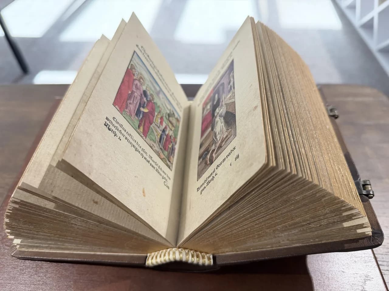 Niewielka otwarta księga z ręcznie kolorowanymi rycinami scen biblijnych.