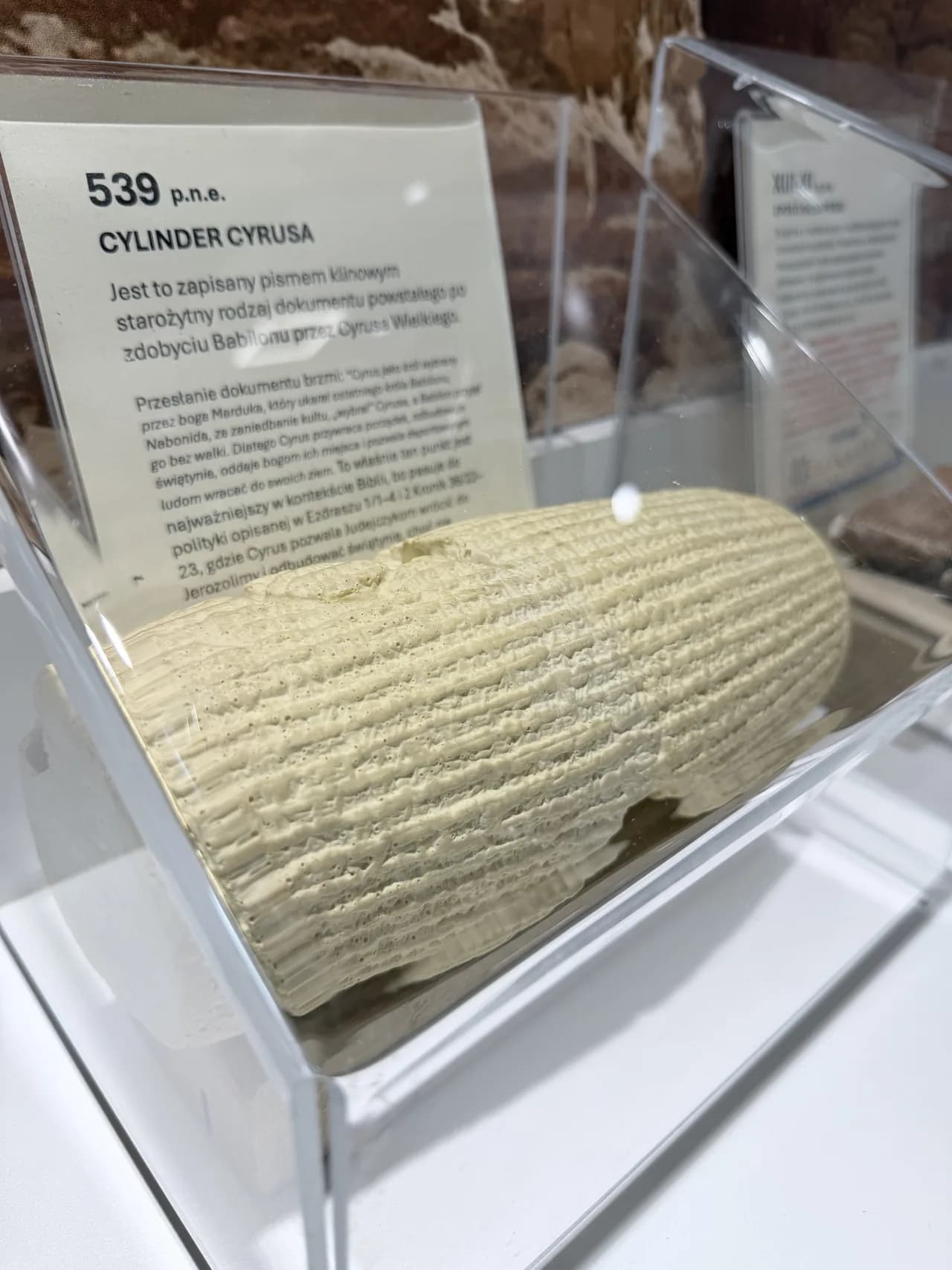 Cylinder Cyrusa z 539 r. p.n.e. w gablocie ekspozycyjnej, za nim tabliczka z opisem.